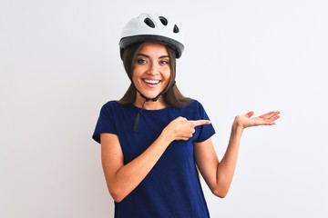Canvas Print - Young beautiful cyclist woman wearing security bike helmet over isolated white background amazed and smiling to the camera while presenting with hand and pointing with finger.