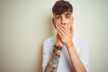 Young man with tattoo wearing t-shirt standing over isolated white background shocked covering mouth with hands for mistake. Secret concept.