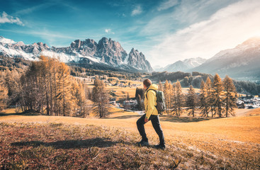 Wall Mural - young man in yellow jacket with backpack is walking on the meadow against the mountains at sunset in