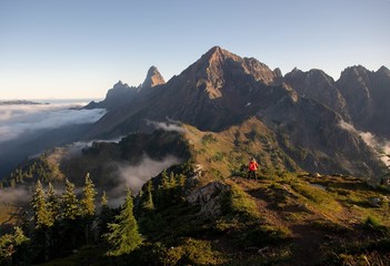 Wall Mural - A woman in a red coat walking on a trail toward mountains 