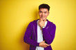 © Krakenimages.com - Young asian chinese man wearing purple sweatshirt standing over isolated yellow background looking confident at the camera smiling with crossed arms and hand raised on chin. Thinking positive.