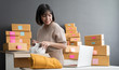 © sutthinon602 - Startup small business SME, Entrepreneur owner using smartphone or laptop taking receive and checking online purchase shopping order to preparing pack product box. Selling online ideas concept