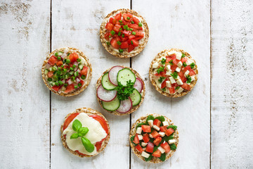 Wall Mural - various healthy sandwiches with rice cake chopped tomatoes radish cucumber basil cheese green onion on white wooden background top view