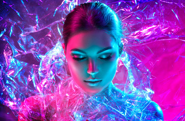 Wall Mural - Fashion model woman in colorful bright neon lights posing in studio through transparent film. Portrait of beautiful sexy girl in UV. Art design colorful makeup