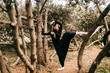 © benevolente - Young beautiful ballerina in black vintage dress with veil posing among trees outdoor.