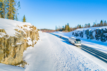 Winter journey. Bus transportation on the winter road. Road safety. Bus on the road. Snow-covered rocks and pines across the road. Trip to Karelia. Stay in the fresh air.