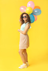 Happy African-American woman with air balloons on color background