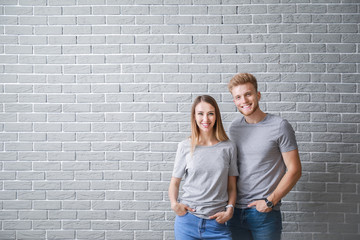 Couple in stylish t-shirts against brick wall