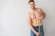 © Pixel-Shot - Handsome muscular man with measuring tape on light background. Weight loss concept