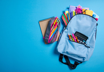 Back to school concept. Blue backpack with school supplies on blue background. Top view. Copy space