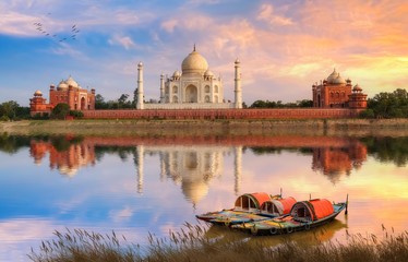 Fototapete - Taj Mahal Agra on the banks of river Yamuna at sunset with moody sky and view of wooden boats used for tourist ride on the river 