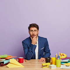 Wall Mural - Amazed hipster guy gazes in stupor, gets unexpeted news, astonished with something, wonders unbelievable offer from colleague, wears glasses and elegant suit, isolated on purple studio wall.