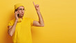 © wayhome.studio - Sad displeased man has telephone conversation, raises index finger up, hears bad news, wears yellow hat and t shirt, gets idea in mind how to improve situation, stands indoor, copy space for your text