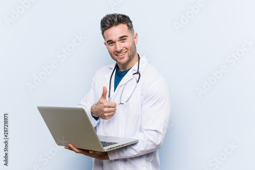Fotografía Caucasian doctor man holding a laptop smiling and raising thumb up