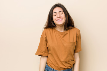 Wall Mural - Young brunette woman against a beige background laughs and closes eyes, feels relaxed and happy.