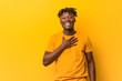 © Asier - Young black man wearing rastas over yellow background laughs out loudly keeping hand on chest.