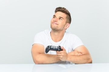 Young man holding a game controller smiling confident with crossed arms.