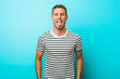 © Asier - Young caucasian man against a blue wall funny and friendly sticking out tongue.