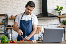 Handsome Caucasian Man Cooking On Kitchen With Laptop On Table