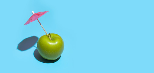 Wall Mural - Concept of fresh green apple with a umbrella isolated on blue background.