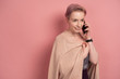 © bestsenny - A girl with short pink hair, smiling, speaks on the phone, hiding behind a cardigan, stands on a pink background.
