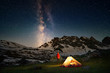 Hiker standing near tent and looking at the milky way in mountains at night