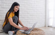 © weedezign - Asian female sit with knees up on floor using laptop on wicker stand near window in living room at home.Work at home concept.work from home.relax lifestyle