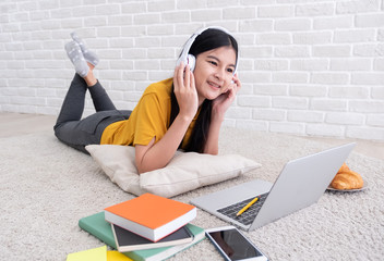 Poster - Asian female listen to music and use laptop computer to work at home.woman lay down on carpet at brick wall.working online lifestyle