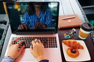 Wall Mural - First person view of female entrepreneur eating breakfast of coffee and pastries and working on laptop