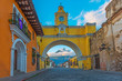 The colorful yellow arch of Antigua city at sunrise with the active Agua volcano in the background, Guatemala.
