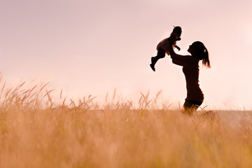 Mother playing with her baby outdoor, silhouette.