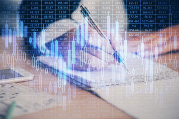 A woman hands writing information about stock market in notepad. Forex chart holograms in front. Concept of research. Multi exposure