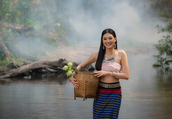 Beautiful woman wearing a northern style dress standing in the stream  with lotus basket, Chiangmai, Thailand.