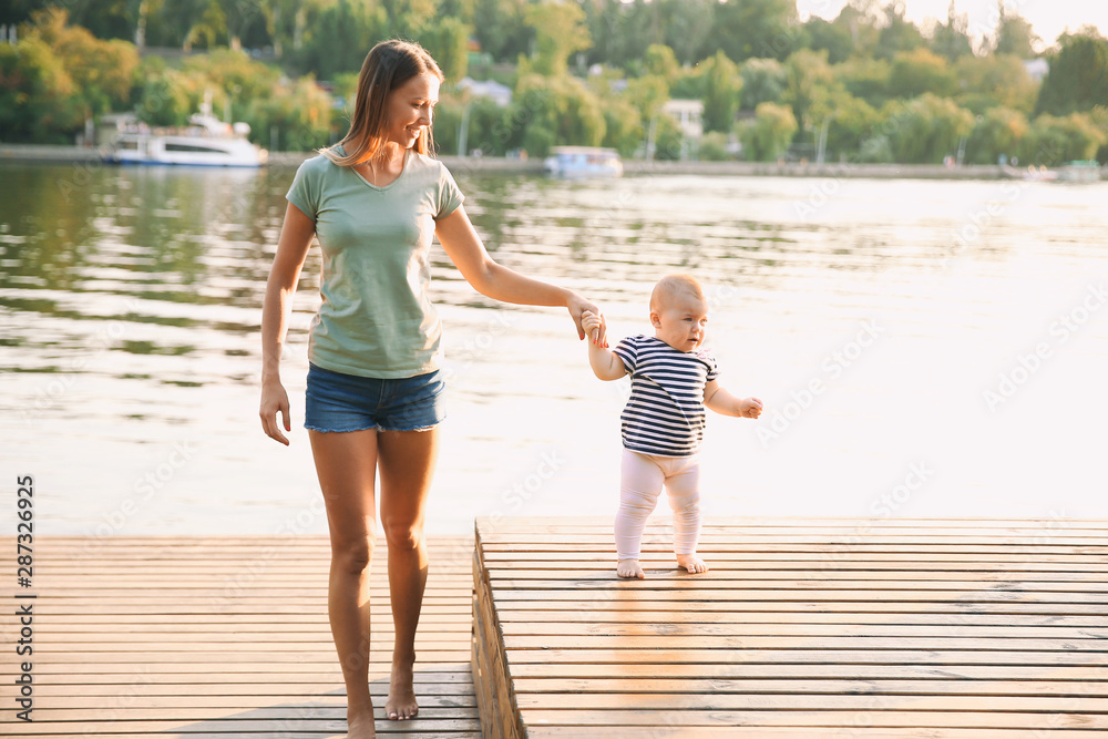 Mother teaching her little baby to walk near river