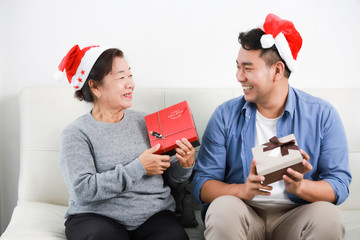 Wall Mural - Asian senior woman mother and young man son in blue shirt give gift box for Christmas gift in living room