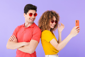 Canvas Print - Portrait of stylish caucasian couple smiling and taking selfie photo on cellphone in trendy sunglasses