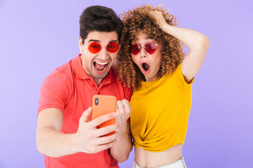 Poster - Portrait of amazed caucasian couple rejoicing and taking selfie photo on cellphone in trendy sunglasses