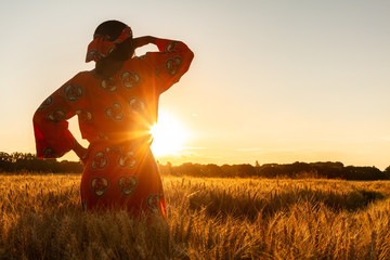african woman in traditional clothes standing in a field of crops at sunset or sunrise