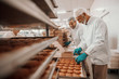© Dusan Petkovic - Two hardworking dedicated Caucasian employees dressed in white sterile uniforms collecting and packing cookies in boxes. Food plant interior.
