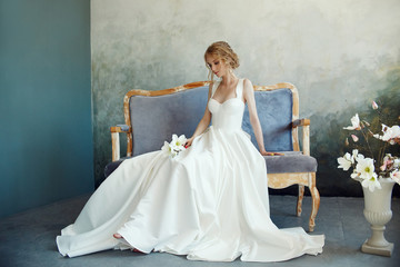 Perfect bride, portrait of a girl in a long white dress. Beautiful hair and clean delicate skin. Wedding hairstyle blonde woman. Girl with a white flower in her hands