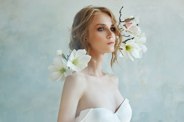 Perfect bride with jewels, a portrait of a girl in a long white dress. Beautiful hair and clean delicate skin. Wedding hairstyle blonde woman. Girl with a white flower in her hands