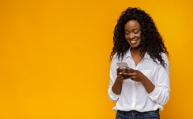 interested african american girl using smartphone on yellow background