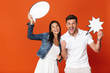 Sticker - Optimistic emotional positive happy loving couple isolated over red wall background holding speech bubbles.