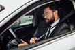 © Тарас Нагирняк - Handsome young serious bearded driver in full suit with fastening seat belt driving a car.