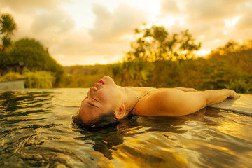 Wall Mural - tropical holidays lifestyle portrait of young beautiful and happy Asian Korean woman in bikini enjoying sunset at amazing jungle resort infinity pool swimming relaxed