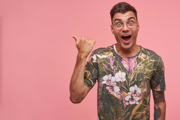 Canvas Print - Indoor shot of excited short haired young man wearing glasses and flowered t-shirt, looking joyfully with surprised face expression, isolated over pink background