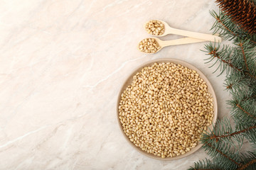 pine nuts on the plate with two spoons, cones, brunches . top view on beige marble table with copy space.