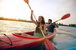 Leinwandbild Motiv Confident young caucasian couple kayaking on river together with sunset in the backgrounds. Having fun in leisure activity. Romantic and happy woman and man on the kayak. Sport, relations concept.