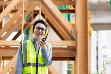 Wall Mural - Image outside the industrial construction engineers in yellow protective ear muff discuss new project while using walkie talkie and happy smile on the open building site near the crane.