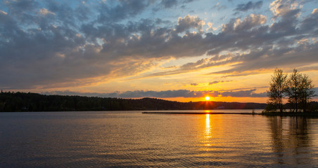 Wall Mural - Amazing sunset in Finland during summer evening. Golden hour and dramatic clouds. Reflection in water, calm scenery.